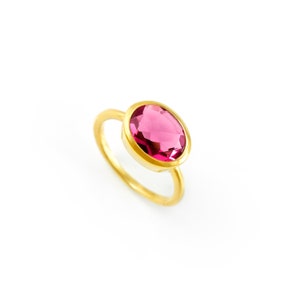 May include: A gold ring with a large, oval-shaped, pink gemstone.