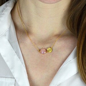May include: A delicate gold chain necklace with a pink gemstone and a gold disc pendant.