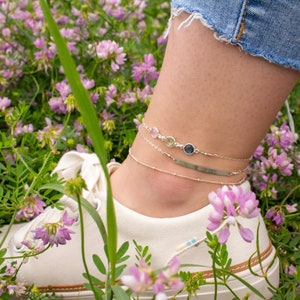 A person wearing a 3-stone anklet, an engravable bar anklet, and a simple satellite chain anklet layered. Layering anklets, minimalist jewelry, layered jewelry, gemstone anklet, sterling silver anklet, gold anklet, birthstone jewelry, mothers anklet