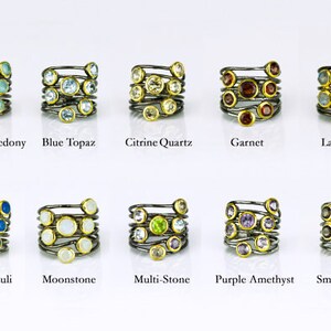 May include: Ten silver rings with gold accents, each featuring a different gemstone. The gemstones are arranged in a spiral pattern on each ring. The gemstones include aqua chalcedony, blue topaz, citrine quartz, garnet, labradorite, lapis lazuli, moonstone, multi-stone, purple amethyst, and smoky quartz.