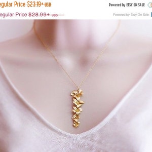 May include: A gold necklace with a delicate pendant featuring a cluster of small, stylized flowers. The pendant is about 2 inches long and hangs from a thin gold chain.