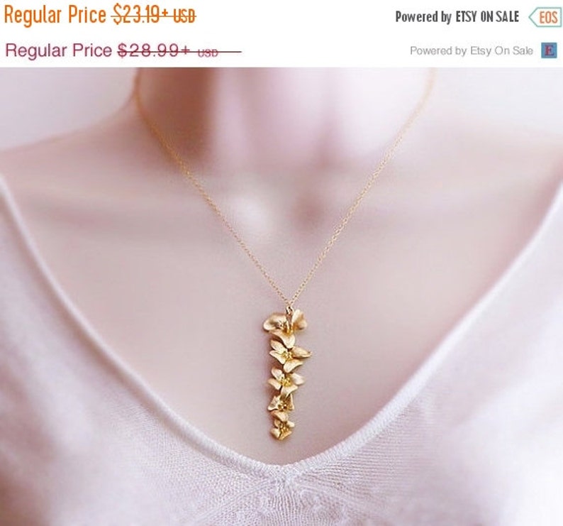 May include: A gold necklace with a delicate pendant featuring a cluster of small, stylized flowers. The pendant is about 2 inches long and hangs from a thin gold chain.