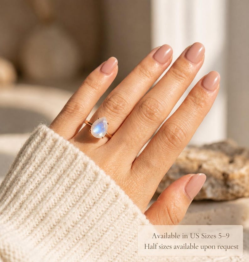 Moonstone teardrop ring worn on hand with text overlay showing available US sizes 5 to 9 and half sizes available upon request. A helpful sizing image for a June birthstone ring, pear gemstone ring, rainbow moonstone ring, and gift for her.