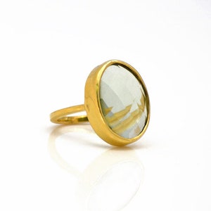 May include: A gold ring featuring a large, oval-shaped, light green gemstone.