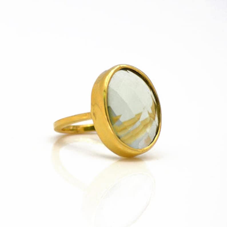 May include: A gold ring featuring a large, oval-shaped, light green gemstone.