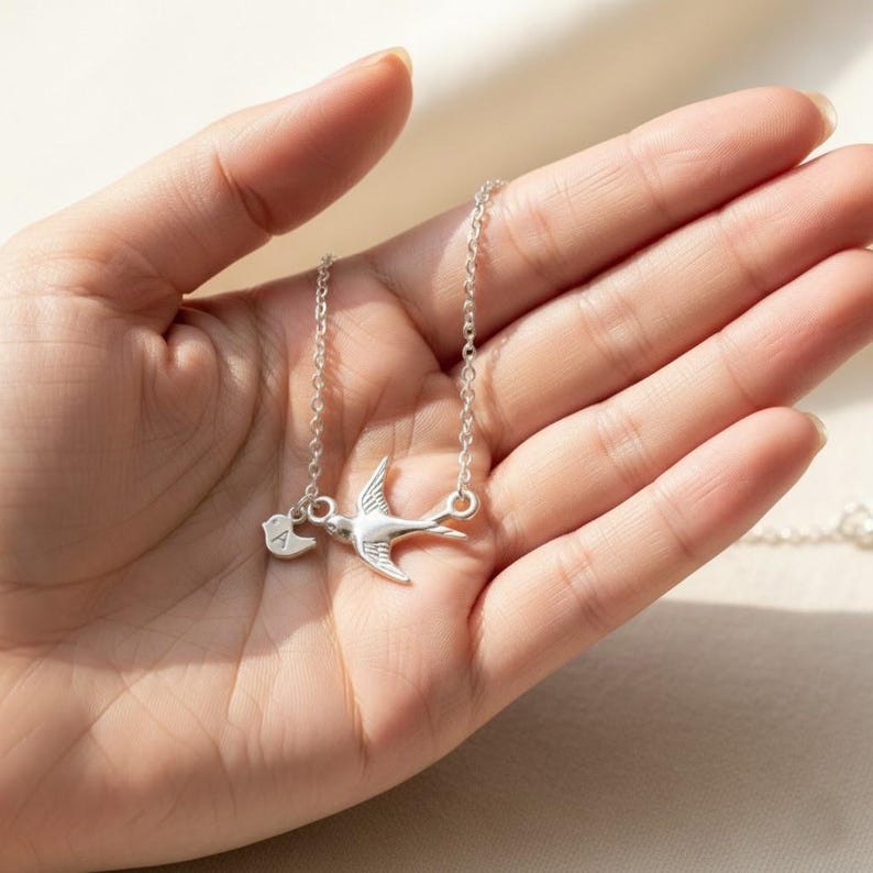Hand-held close-up of silver mama bird necklace with engraved baby bird initials, personalized family keepsake jewelry for mom, grandma, or new mother gift.