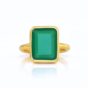 Könnte beinhalten: Ein goldener Ring mit einem grünen Edelstein, der in einer quadratischen Form gefasst ist.