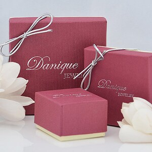 May include: Three red boxes with the text "Dannique Jewelry" printed on them. The boxes are tied with silver ribbon and are sitting on a white surface.