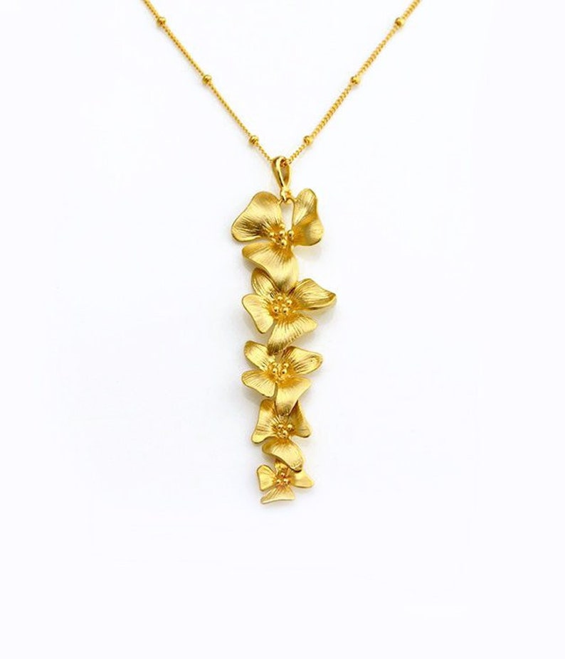 May include: A gold necklace with a pendant featuring a cluster of five delicate, gold-toned flower charms. The flowers are arranged vertically, creating a cascading effect.