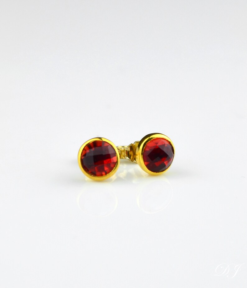 May include: A pair of gold stud earrings with red gemstone accents.