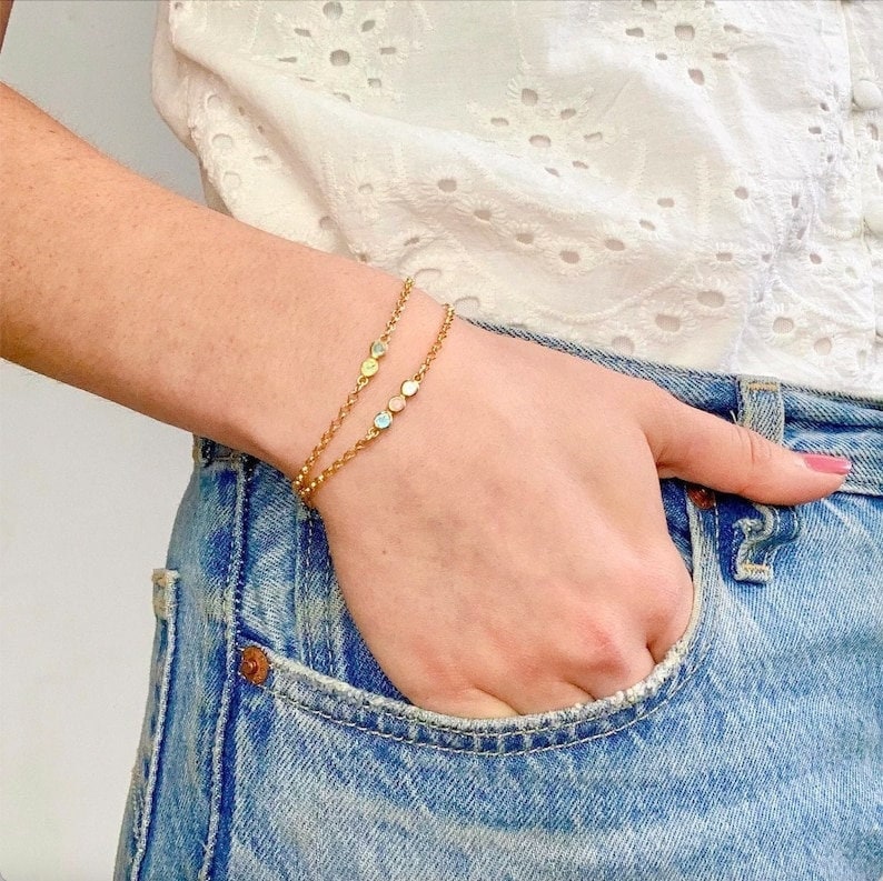 A model in a white shirt has her hand in her pocket and wears two birthstone bracelets. These bracelets are perfect for women, grandma, mom, birthstone friendship bracelets. Easy to clasp and durable, these pieces of jewelry last for years to come.