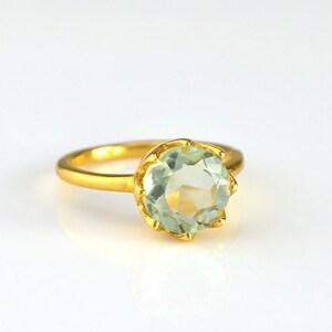 Op de afbeelding: Een gouden ring met een grote, ronde, lichtgroene edelsteen in een kroonvormige zetting.