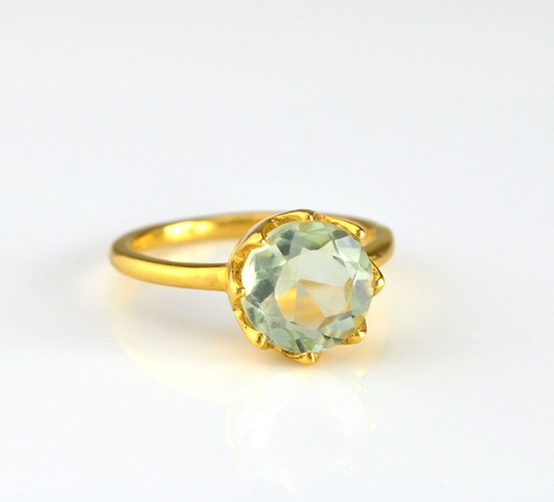 Op de afbeelding: Een gouden ring met een grote, ronde, lichtgroene edelsteen in een kroonvormige zetting.