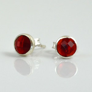 May include: A pair of silver stud earrings with red oval-shaped gemstones.