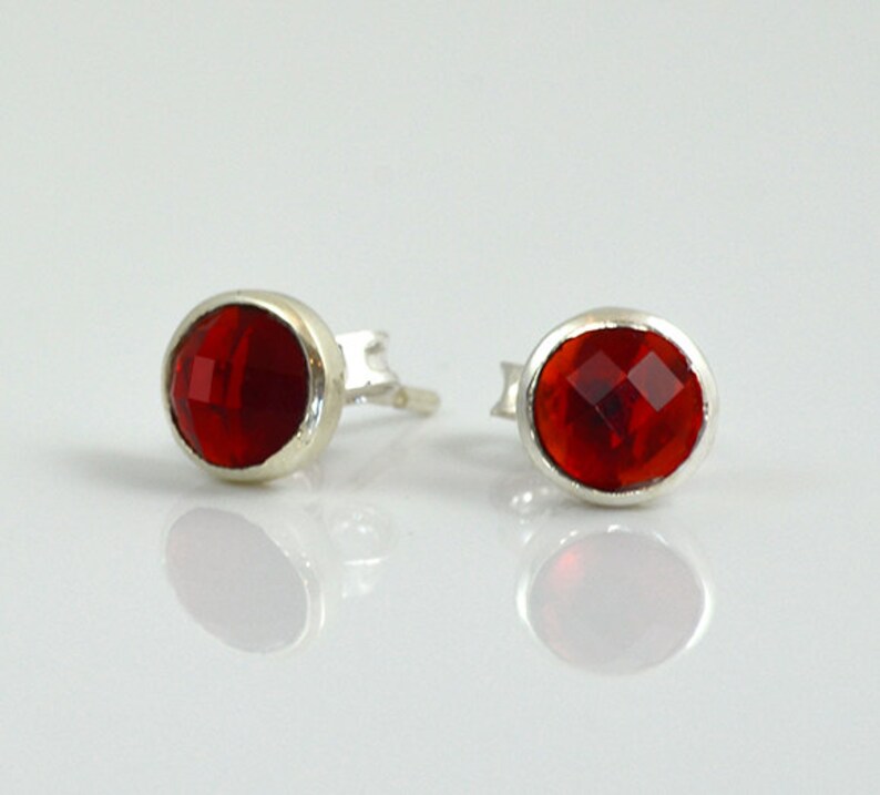 May include: A pair of silver stud earrings with red oval-shaped gemstones.