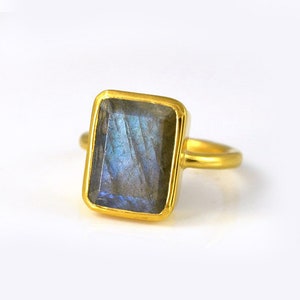 May include: A gold ring with a large, rectangular, iridescent blue labradorite gemstone.