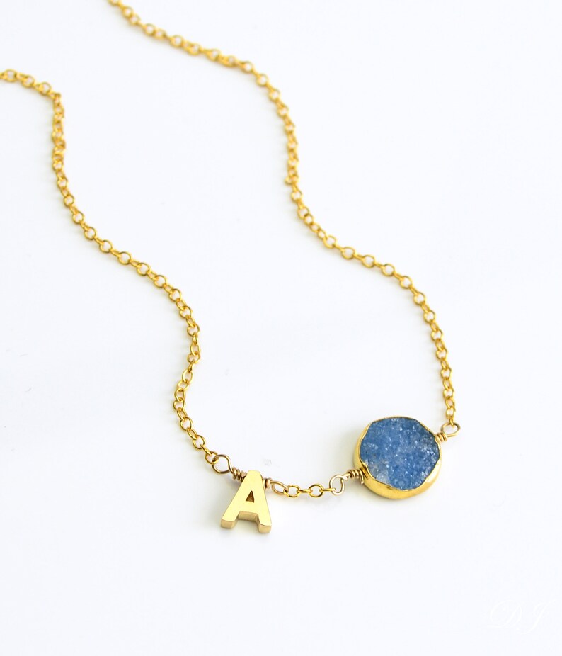 K&ouml;nnte beinhalten: Eine goldene Kettenkette mit einem Anh&auml;nger aus blauem Achat und einem goldenen Buchstaben 'A' als Anh&auml;nger.