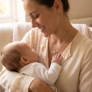 Lifestyle photo of mom holding baby while wearing personalized bird necklace, sentimental motherhood jewelry featuring initial charms representing children.