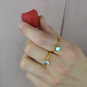 Op de afbeelding: Twee gouden ringen met edelsteen bezetting. De ring aan de linkerkant heeft een lichtblauwe edelsteen, en de ring aan de rechterkant heeft een donkerblauwe edelsteen.