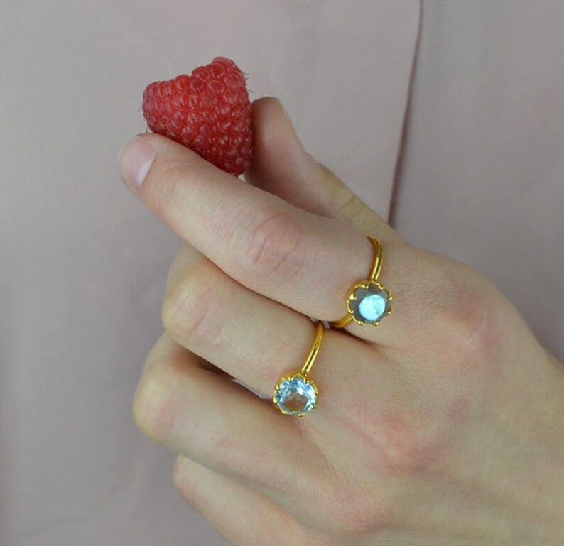 Op de afbeelding: Twee gouden ringen met edelsteen bezetting. De ring aan de linkerkant heeft een lichtblauwe edelsteen, en de ring aan de rechterkant heeft een donkerblauwe edelsteen.