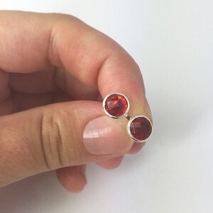 May include: A pair of silver stud earrings with red gemstone accents.
