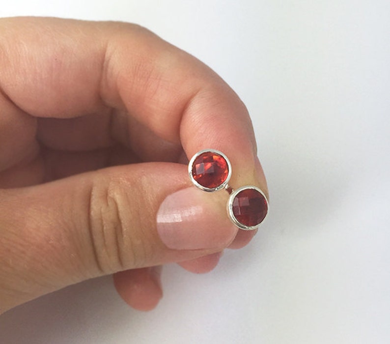 May include: A pair of silver stud earrings with red gemstone accents.