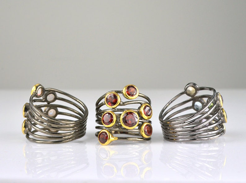 May include: Three silver rings with multiple bands and colorful gemstones. The rings are set on a white surface.