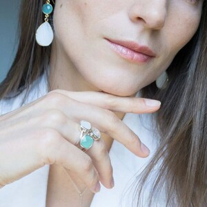 May include: A silver ring with three square-shaped gemstones. The ring features a light blue gemstone, a white gemstone, and a clear gemstone.