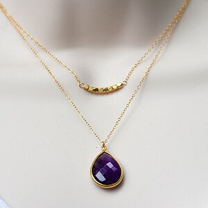 Pode incluir: Um colar de corrente de ouro com um pingente de pedra preciosa de cor p&uacute;rpura em forma de l&aacute;grima e uma corrente de ouro menor com uma fila de contas douradas.