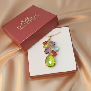 grandma birthstone necklace in Danique Jewelry gift box, featuring a cascading family pendant with multiple faceted teardrop gemstones in green, red, purple, blue and peridot tones set in gold, displayed on soft champagne satin, sentimental multi birthstone necklace that can represent grandchildren or children, perfect gift for grandma or mom for Mother’s Day, birthday, Christmas or milestone celebrations, ready for gifting in branded red jewelry box