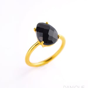 May include: A gold ring with a black gemstone. The gemstone is a teardrop shape and has a faceted cut.