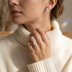 Model wearing moonstone teardrop ring and matching earrings with cream sweater, showing the soft blue flash of rainbow moonstone. A June birthstone jewelry look, gift for her, everyday gemstone ring, birthday gift, or delicate statement ring.