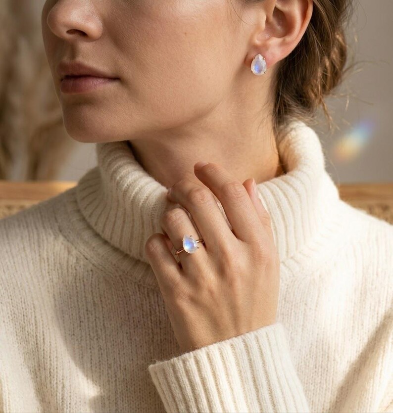 Model wearing moonstone teardrop ring and matching earrings with cream sweater, showing the soft blue flash of rainbow moonstone. A June birthstone jewelry look, gift for her, everyday gemstone ring, birthday gift, or delicate statement ring.