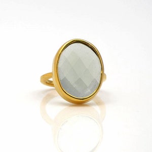 May include: A gold ring featuring a large, oval-shaped, faceted, white gemstone.