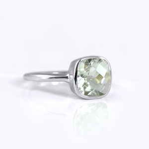 May include: A silver ring with a light green square-shaped gemstone.