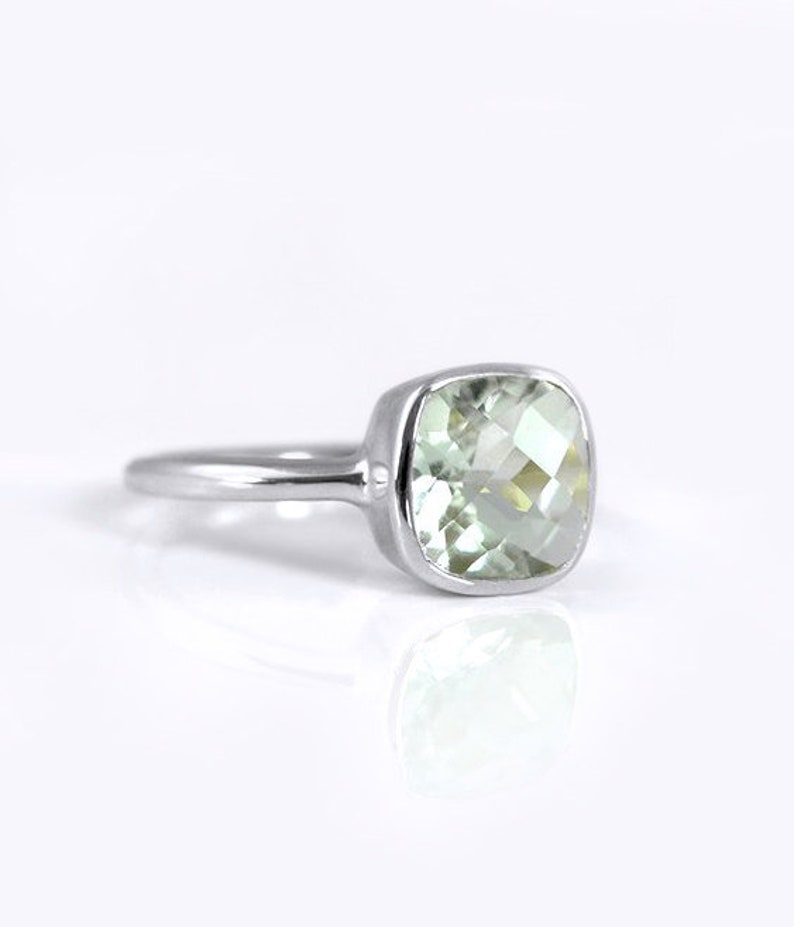 May include: A silver ring with a light green square-shaped gemstone.