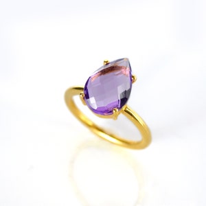 May include: A gold ring with a purple amethyst gemstone in a teardrop shape.