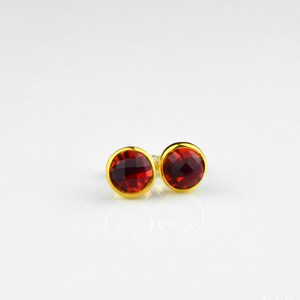 May include: A pair of gold stud earrings with red gemstone accents.