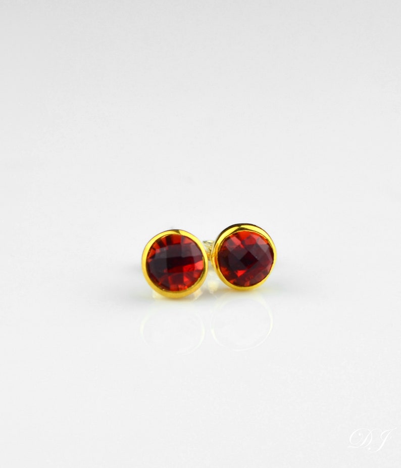 May include: A pair of gold stud earrings with red gemstone accents.