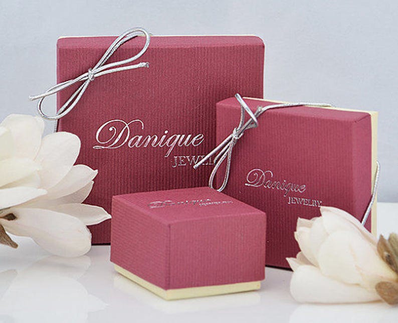 May include: Three red gift boxes with silver ribbon and the text "Dannique Jewelry" printed on the front.