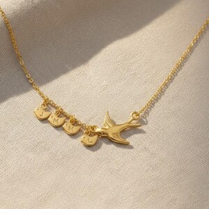 Model in blue top wearing gold mama bird necklace, everyday fashion styling for personalized family jewelry, initial baby bird charms as a keepsake.