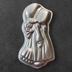 May include: A silver-colored metal cake pan in the shape of a bonneted woman. The pan has detailed features, including a bow, sleeves, and a skirt. The pan is designed for baking cakes in a unique, decorative shape.