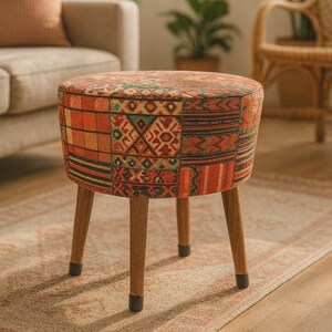 May include: A round ottoman featuring a patchwork fabric upholstery with a multi-colored geometric pattern in shades of orange, red, green, and black. The piece is supported by four tapered wooden legs with dark protective caps on the feet.