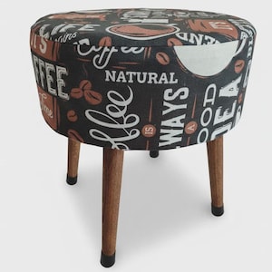 May include: A round stool with three tapered wooden legs and black rubber feet. The seat features a black fabric cover with a repeating coffee-themed print in white and brown, including text such as Coffee is always a good idea and Natural.