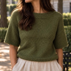 May include: An olive green short-sleeved sweater featuring a ribbed knit texture, a wide crew neckline, and a straight hemline. The garment is constructed with a consistent vertical rib pattern throughout the body and sleeves, providing a structured fit.