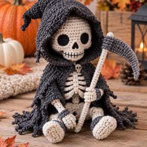 Pode incluir: Uma figura de esqueleto em crochê vestindo uma capa com capuz cinza-escuro com um pequeno botão de caveira no pescoço. A figura tem um corpo de fio cor de creme e segura uma foice de crochê com um cabo longo. Detalhes da caixa torácica visíveis.