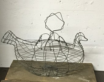 May include: A wire chicken shaped basket with a round base and a wire crown on top. The basket is sitting on a wooden surface.
