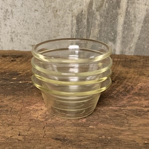 May include: Three clear glass ramekins stacked on top of each other on a wooden surface.