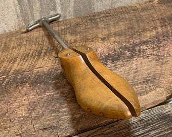 May include: A wooden shoe stretcher with a metal handle. The stretcher is designed to help maintain the shape of shoes and prevent wrinkles.