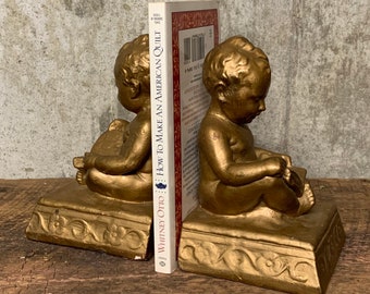 May include: A pair of gold cherub bookends holding a book titled "How to Make an American Quilt" by Wendy Otto.
